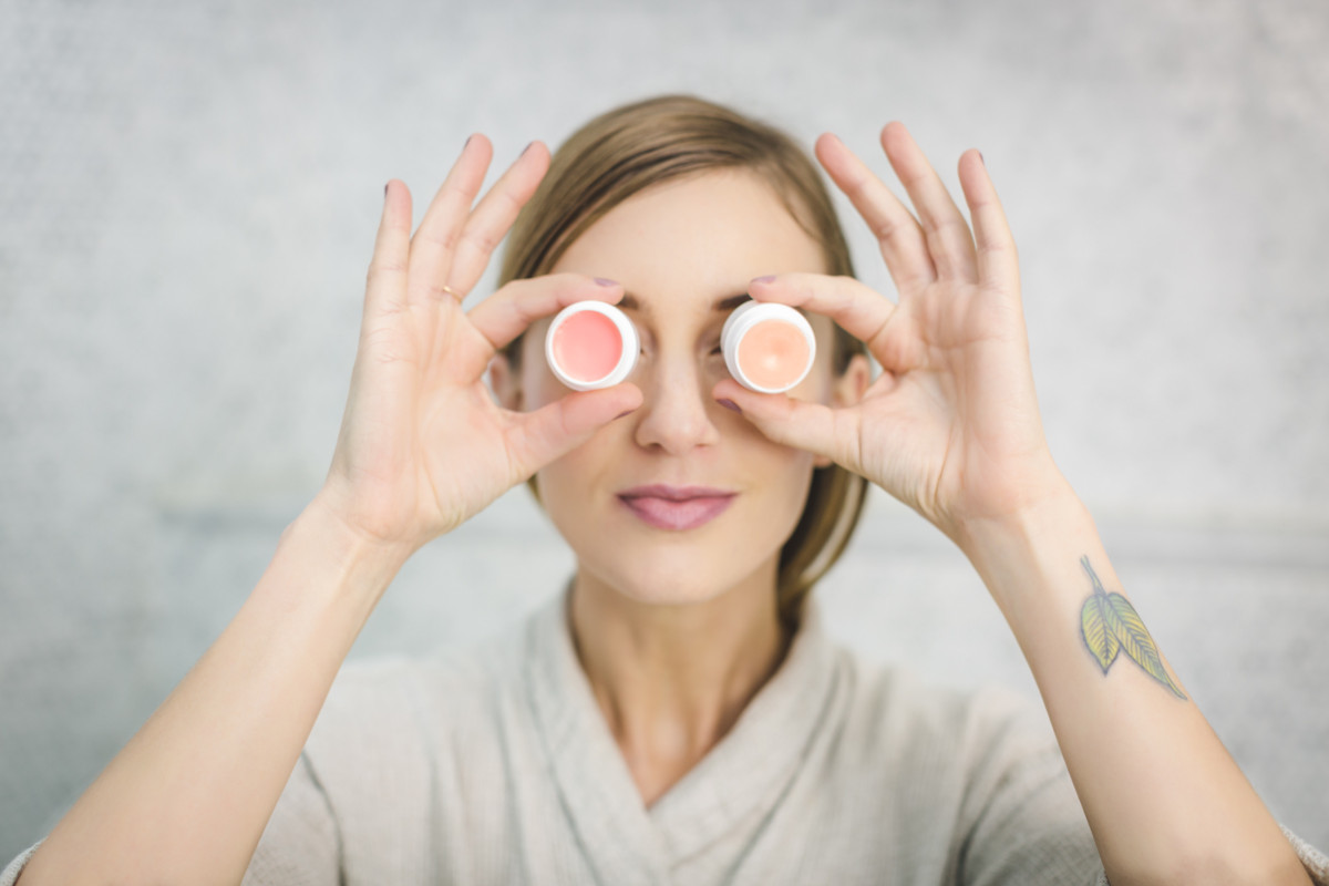 Femme avec 2 pots de crème devant les yeux